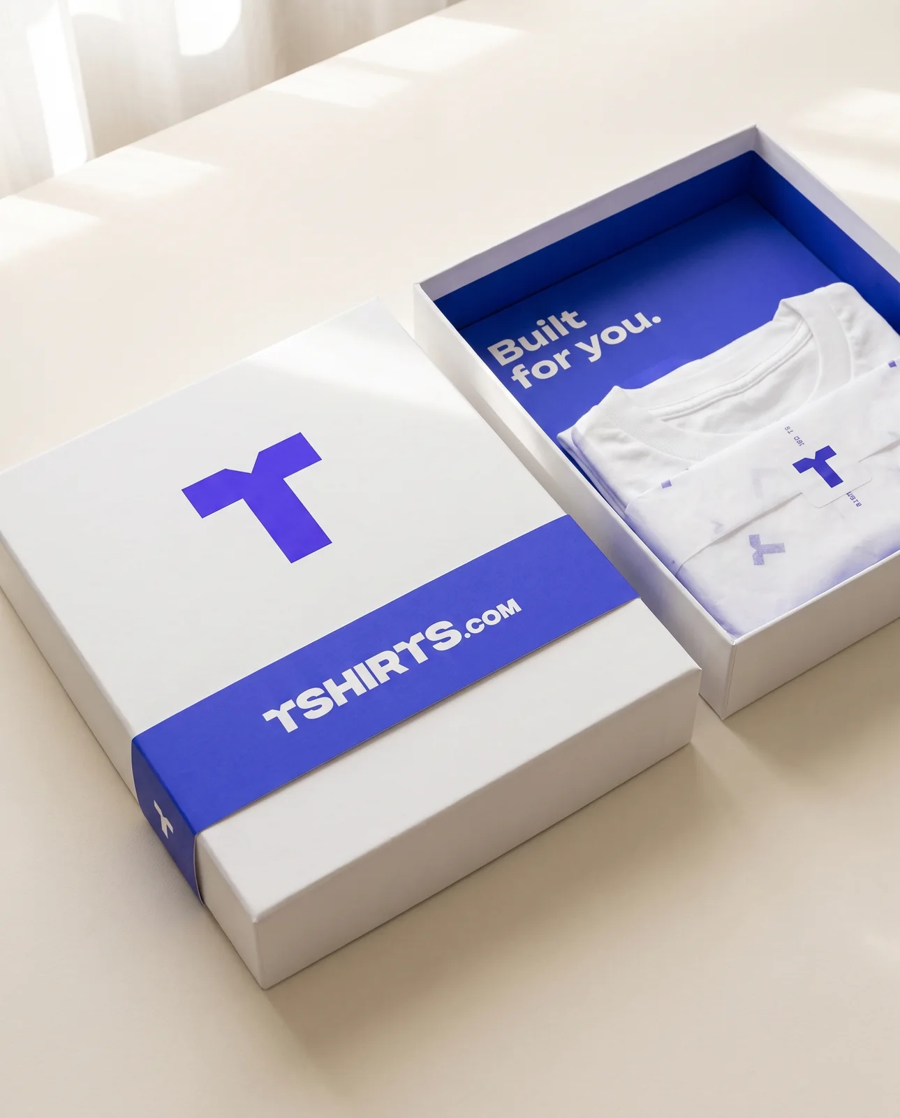 White rigid TSHIRTS.com gift box with an electric-blue T and belly band