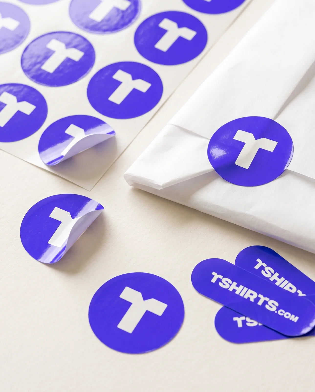 Round electric-blue T seals and TSHIRTS.com wordmark pill stickers
